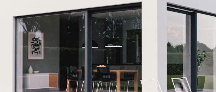 Grandi vetrate scorrevoli con telaio antracite su facciata bianca, vista su sala da pranzo con tavolo in legno e sedie nere